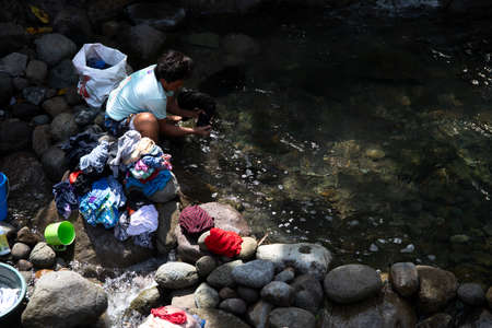 Dumaguete, the Philippines - 23 Jan 2021: woman washing clothes in river. Rustic village lifestyle in South Asia. Household duties on woman. Tough life conditions in asian village. Female daily shoresのeditorial素材