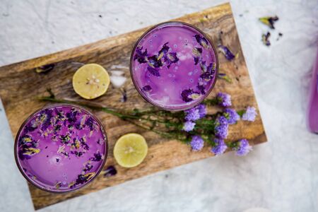 Fresh Lavender Drink with Lemon and Lavender Flowers. Cold Summer Violet Lemonade, Top View on a Wooden Board with lemon pieces and lavender flower. Concept Shot. Violet or Purple Summer Drink.の写真素材