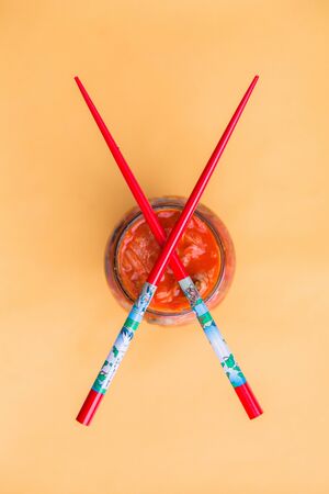 Crossed Red Chopsticks on Kimchi Jar, Top View on Yellow Background. Probiotic Fermented Cabbage Kimchi.の写真素材