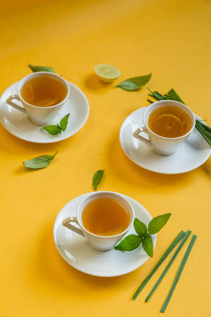 Herbal green tea with lemongrass in glass cup with fresh limes. Top view of three white cups of Lemon Grass Drink on a Yellow Background.の写真素材