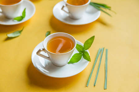 Herbal green tea with lemongrass in glass cup with fresh limes. Top view of three white cups of Lemon Grass Drink on a Yellow Background.の写真素材