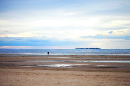 Two people on the sandy beach in cloudy weather, sunsetの写真素材