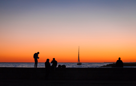 Silhouettes of group of people and yacht with a big sail on the sea as background, nightの写真素材