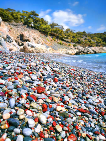 A pebble beach with colored round pebbles, day, sea surf, pines as backgroundの写真素材