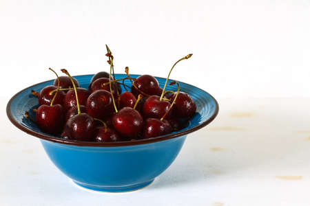 handful cherries in a blue ceramic plate on white wooden background.の写真素材