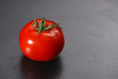 one red fresh tomato with green stem on black backgroundの写真素材