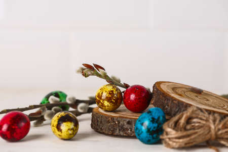 colored quail eggs for Easter and willow branches on white wooden table