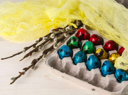 colored quail eggs for Easter in a box with willow branches