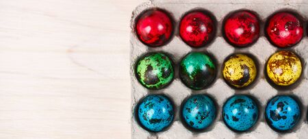 colored quail eggs for Easter in a box on white wooden table