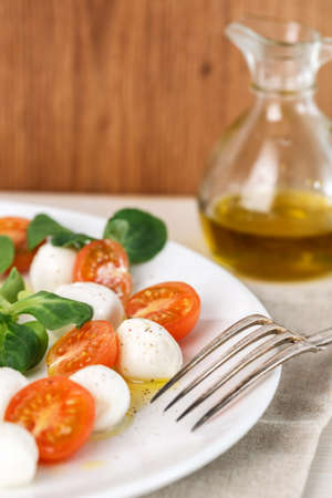 classic Italian Caprese salad with tomato cherry, salad corn on white plate. Textile decoratedの写真素材