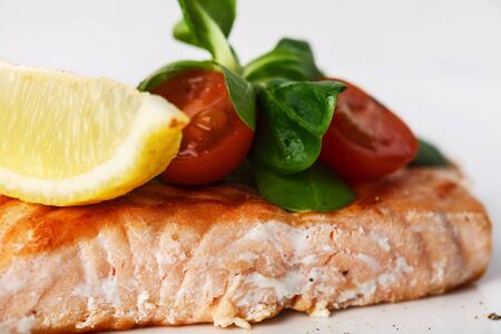 grilled salmon with cherry tomatoes, salad and lemon on white background. Closeup