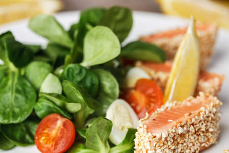 salad with salmon grilled in sesame seeds, cherry tomatoes and quail egg on white plateの写真素材