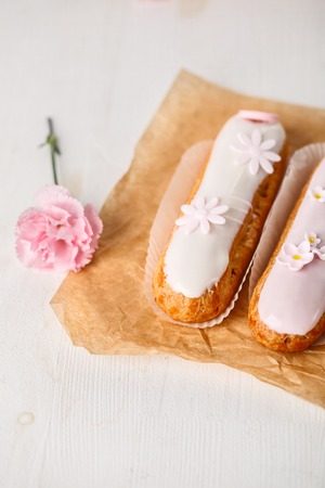 Traditional french eclairs on white table with pink flowerの写真素材
