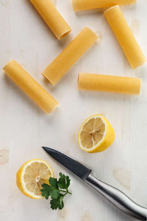 raw Italian pasta cannelloni with lemon on white wooden background with metal knife. Flat layの写真素材