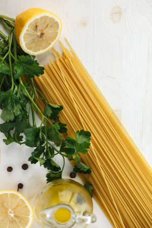 Raw Italian pasta spaghetti with green leaves, lemon, olive oil and spices on white wooden background. Flat lay. Copyspaceの写真素材