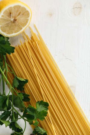 Raw Italian pasta spaghetti with green leaves, lemon, olive oil and spices on white wooden background. Flat lay. Copyspaceの写真素材