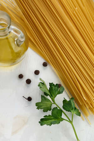 Raw Italian pasta spaghetti with green leaves, lemon, olive oil and spices on white wooden background. Flat lay. Copyspaceの写真素材
