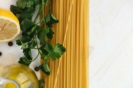 raw Italian pasta spaghetti with green leaves, lemon, olive oil and spices on white wooden background. Flat lay. Copyspaceの写真素材
