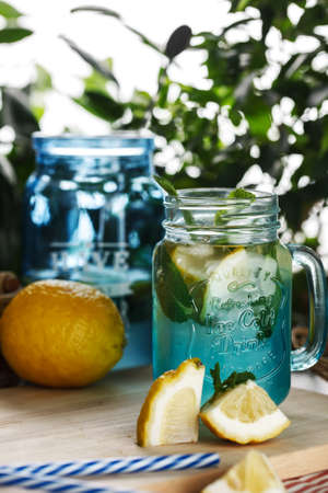 Citrus lemonade water with lemon sliced , healthy and detox water drink in summer on wooden table on a background green foliageの写真素材