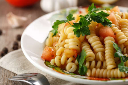 Vegetarian vegetable pasta Fusilli with tomato, parsley and olive oil in white plate on wooden table.の写真素材