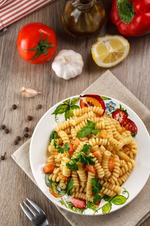 Vegetarian vegetable pasta Fusilli with tomato, parsley and olive oil in white plate on wooden table. Top viewの写真素材