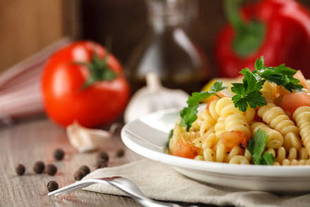Vegetarian vegetable pasta Fusilli with tomato, parsley and olive oil in white plate on wooden table.の写真素材