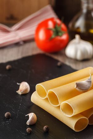 raw cannelloni pasta on black plate on vegetables background for cookingの写真素材