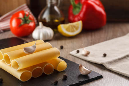raw cannelloni pasta on black plate on vegetables background for cookingの写真素材