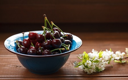 fresh cherries in a blue bowl with wild flowers On a wooden windowsillの写真素材