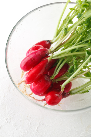 fresh harvest of young radishes with tops in glass bowl on white baclgroundの写真素材
