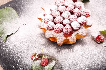 muffin decorated with fresh raspberries on a black plate. All sprinkled with powdered sugar and decorated with green leavesの写真素材