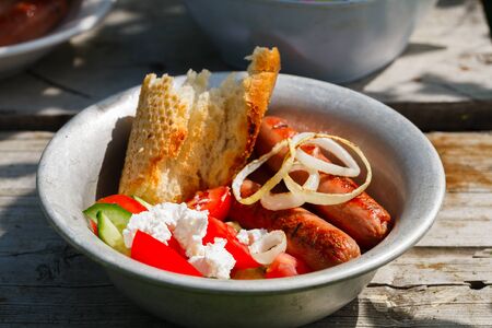 BBQ. Village lunch. grilled sausages with vegetable salad, onion and bread. In a metal plate, on a...