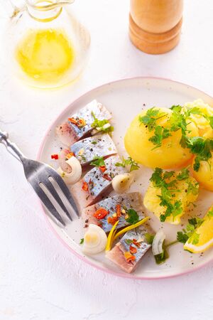 pieces of salted herring in spices with boiled potatoes, lemon and herbsの写真素材