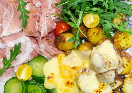 A plate of snacks. Parma ham, pickles, cherry tomatoes, arugula, fried potatoes and raclette cheese