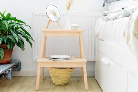 bedside table with a small round mirror, face cream in a white interior next to the bed. Scandinavian styleの写真素材