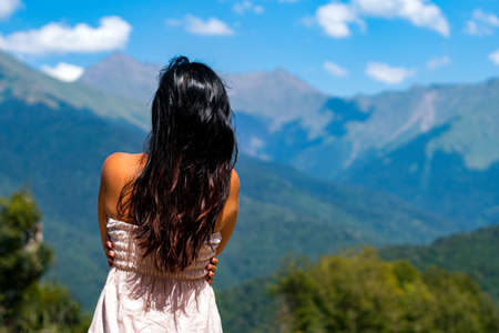 the girl stands against the background of mountains and blue sky, hugging herself. Travel after the pandemic. The mood of loneliness.の写真素材