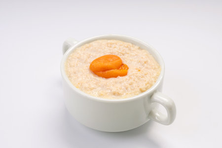 Breakfast. Oatmeal porridge with apricot on a white plate and a white backgroundの写真素材