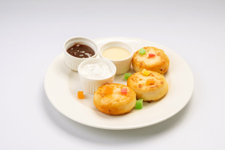 Breakfast. Cheesecakes with sauces and dried fruits on a white plate and a white background.の写真素材