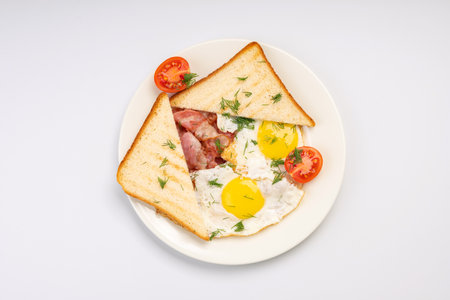 Breakfast. Fried eggs with bacon, toast and tomato on a white plate and a white background.の写真素材