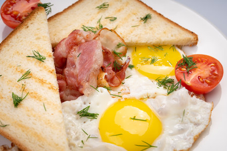 Breakfast. Fried eggs with bacon, toast and tomato on a white plate and a white background.の写真素材