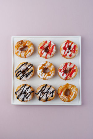 donuts with powdered sugar and various toppings on a white plate on a pale purple background. Top view. Copy spaceの写真素材