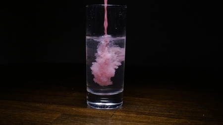 pink paint in a glass of water against a dark backgroundの写真素材