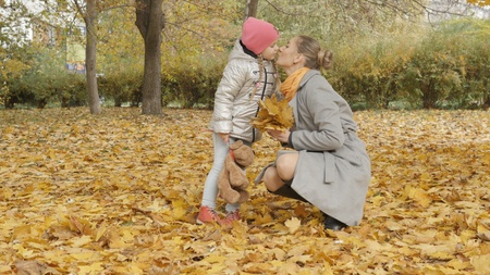 Mom and baby collect yellow fallen leaves in the parkの写真素材