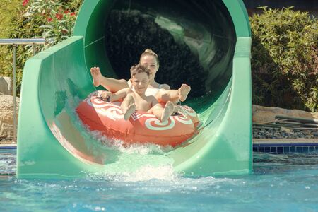 Mother and son are going in a rubber ring down slide at waterpark.