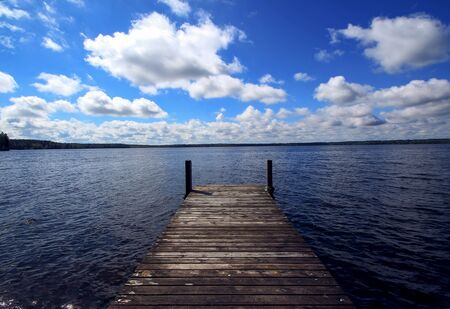 old aged dock in huge blue water lake and taiga forest on background with clouds and deep blue skyの写真素材