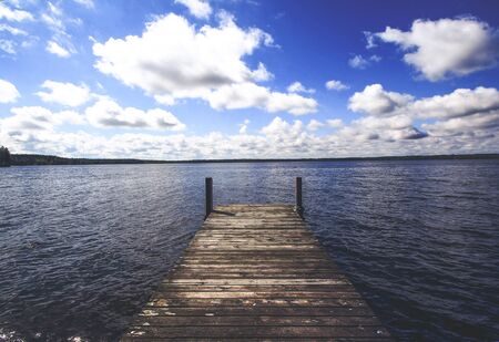 old aged dock in huge blue water lake and taiga forest on background with clouds and deep blue skyの写真素材