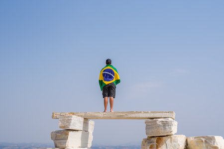 A faraway view of a man standing on a huge pile of flat rocks, looking to Horizon with Brazilian Flag.の写真素材