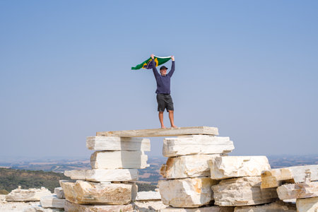 A faraway view of a man standing on a huge pile of flat rocks, looking to Horizon with Brazilian Flag.の写真素材