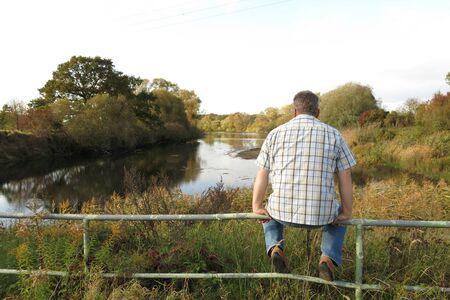 Middle-aged Man Sitting Countryside looking at nature lake and treeの写真素材