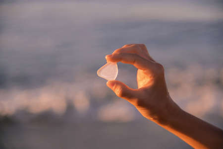 girl holds in her hand a rounded glass from the sea at sunrise on the background of a blurred sea....